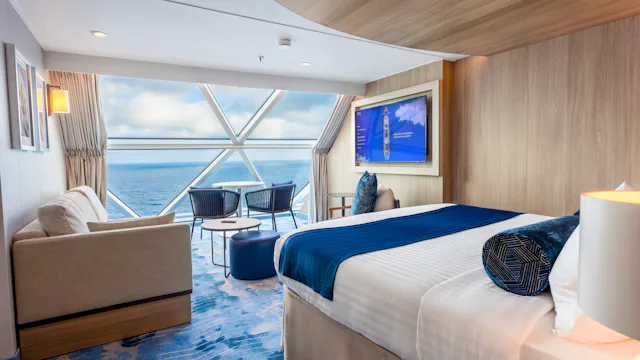 A bed looks out over a living area to panoramic sea view glass windows