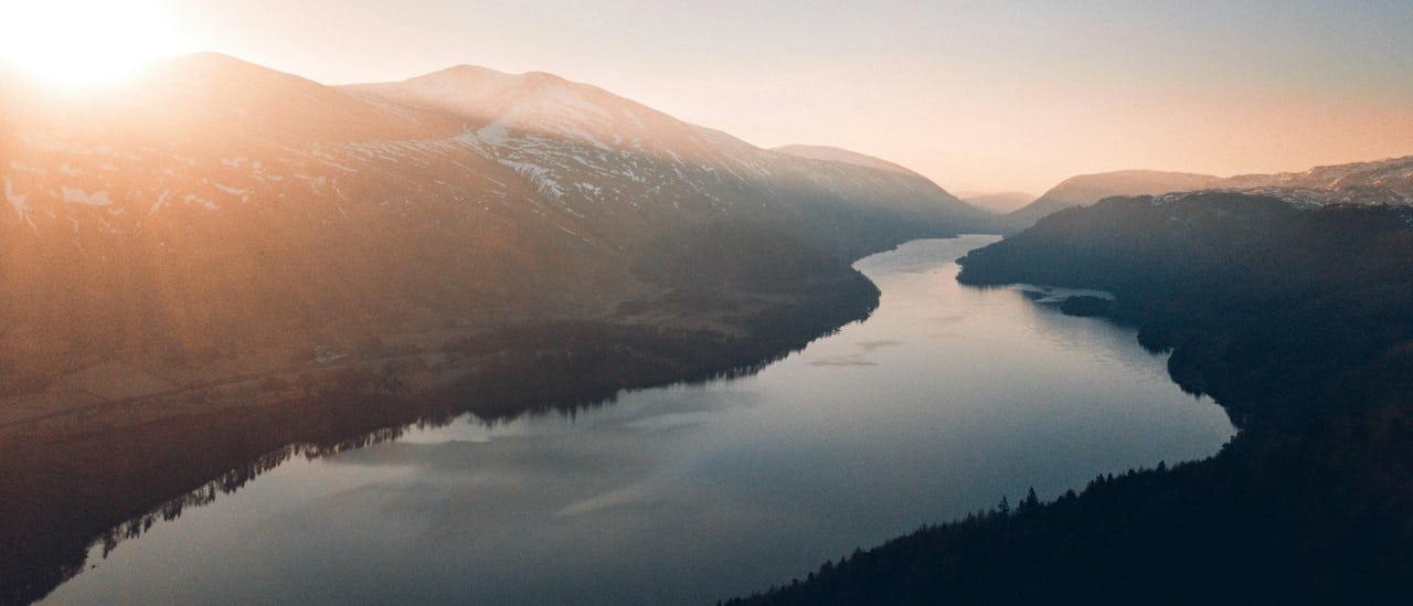 Scenic aerial view of a nile river at sunrise, featuring forested valleys and calm waters reflecting the soft morning light.